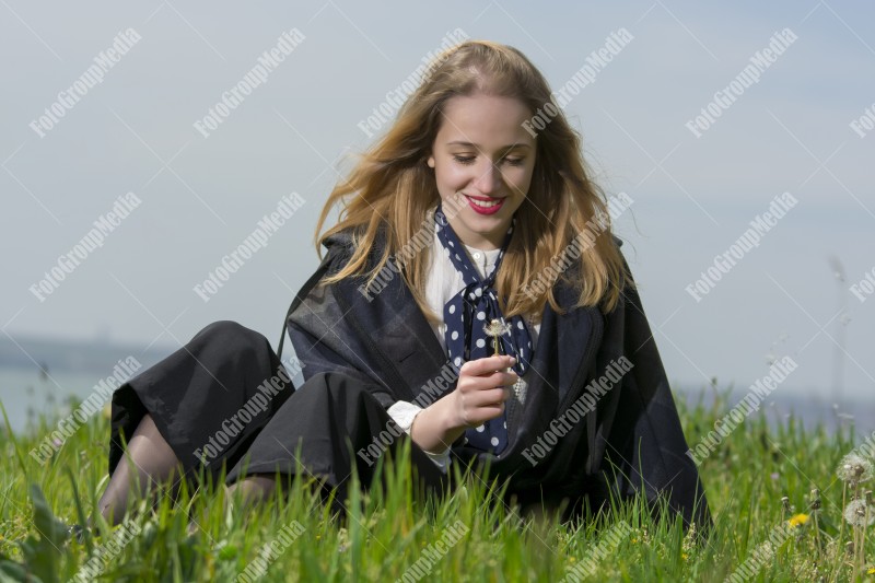 Young girl sitting on grass and playing with dandelion