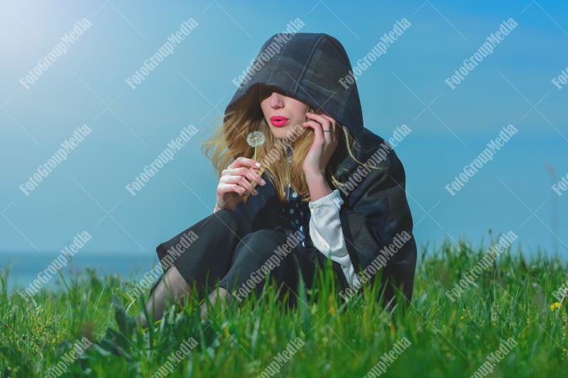 Young girl sitting on grass and playing with dandelion