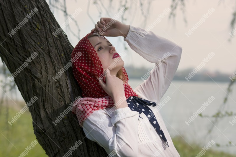 Blonde woman covered with a polka dots red scarf on a tree trunk