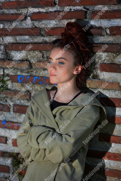 Redhead with blue eyes posing outdoor near a brick wall