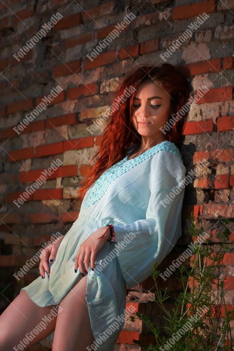 Redhead with blue eyes posing outdoor near a brick wall