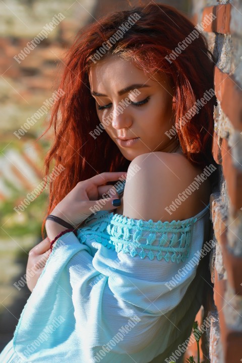 Redhead with blue eyes posing outdoor near a brick wall