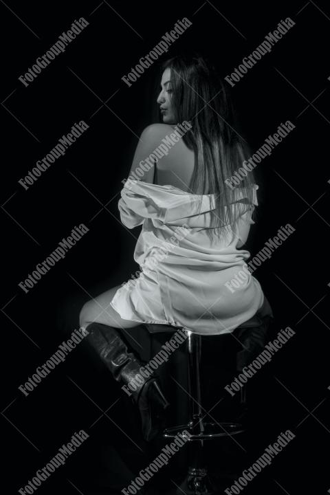A brunette woman sit on the stool, her posture relaxed but alert